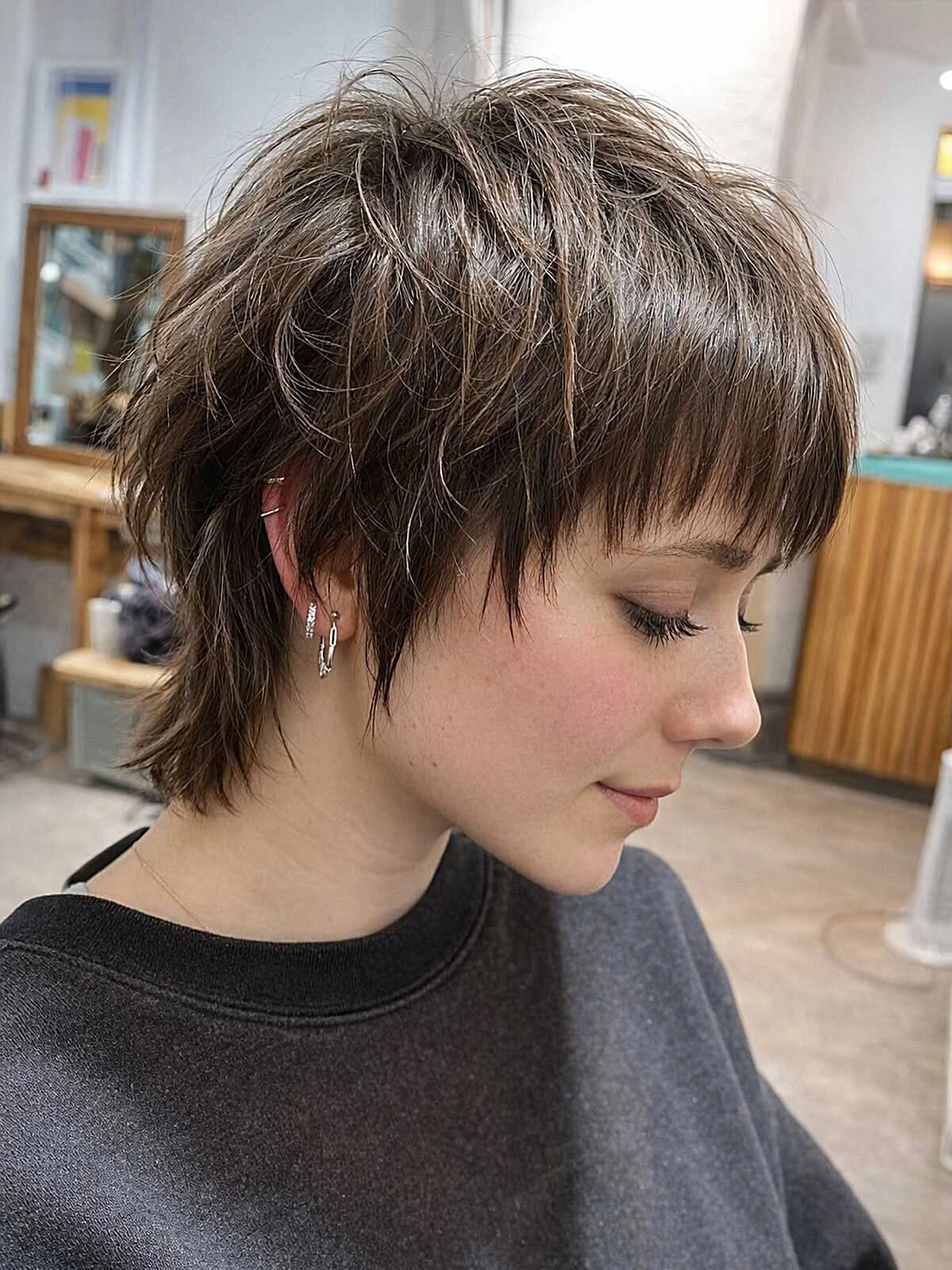 Каштановая слоистая стрижка «пикси» с удлиненной затылочной частью на шее и прозрачной челкой, вид в профиль