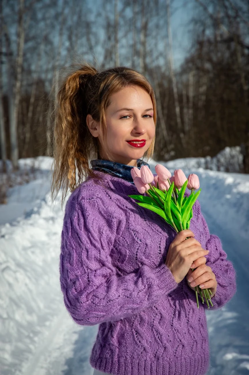 Лиловый свитер с косами и ажурными узорами и темно-синий платок под горловиной на фоне снега